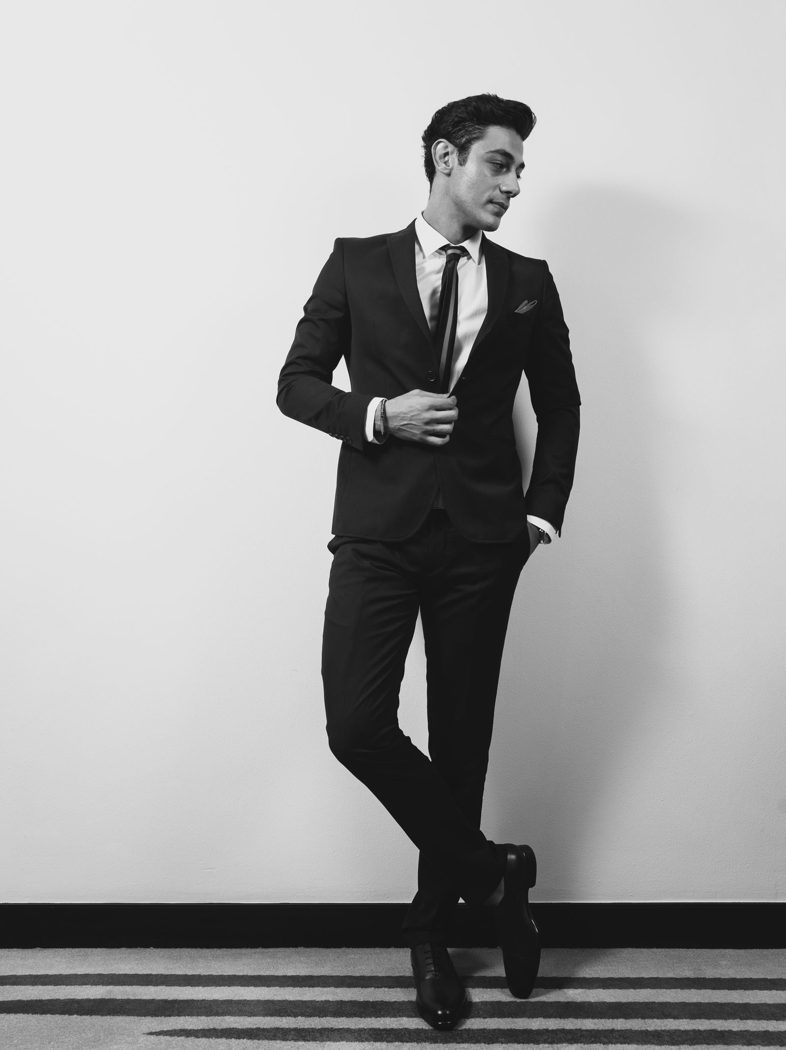 Black and white studio portrait of a man in tailored suit jacket and dress trousers