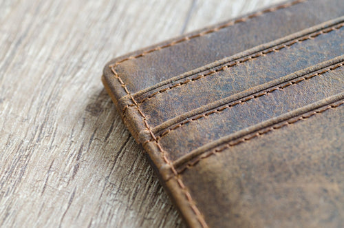 Detailed close-up of a brown leather bifold wallet showing fine stitching